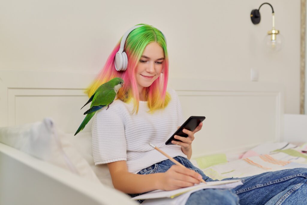 Girl student teenager sitting at home on bed with pet parrot on shoulder