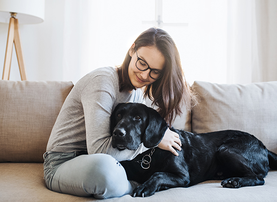 Teenage girl sitting on a sofa indoors, playing with a pet dog.