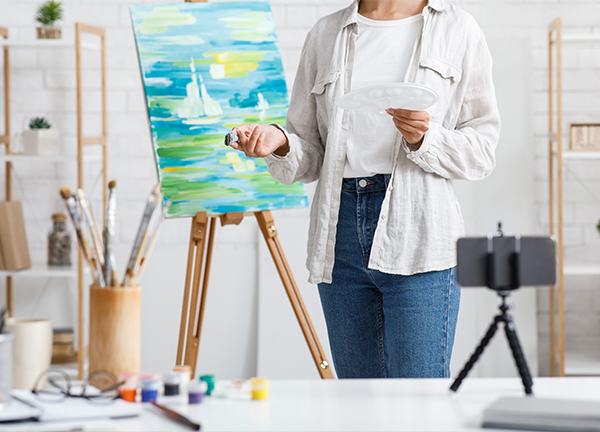 Painting and modern technology. Girl with brushes and paints painting at home